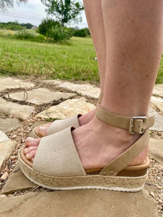 Individual standing on a stone pathway, donning espadrille sandals with ankle straps