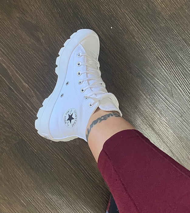 Reviewer wearing high-top white Converse sneakers with a star logo, paired with burgundy pants