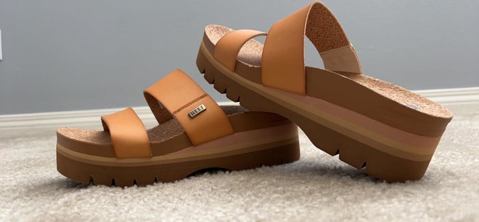 Close-up shot of wedge platform sandals featuring thick straps and a textured sole, resting on a carpeted surface
