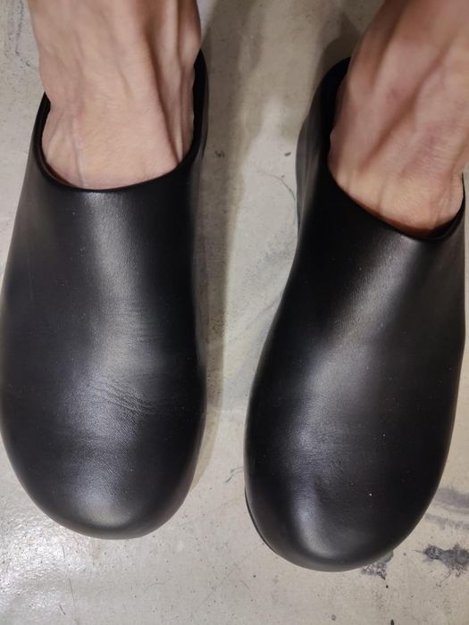 A close-up shot of a person’s feet wearing sleek, minimalist black mules on a concrete floor, ideal for style or shopping content.