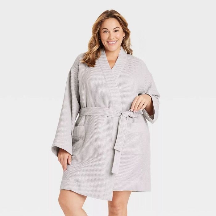 A smiling person modeling a waffle-knit bathrobe with front pockets and a belt