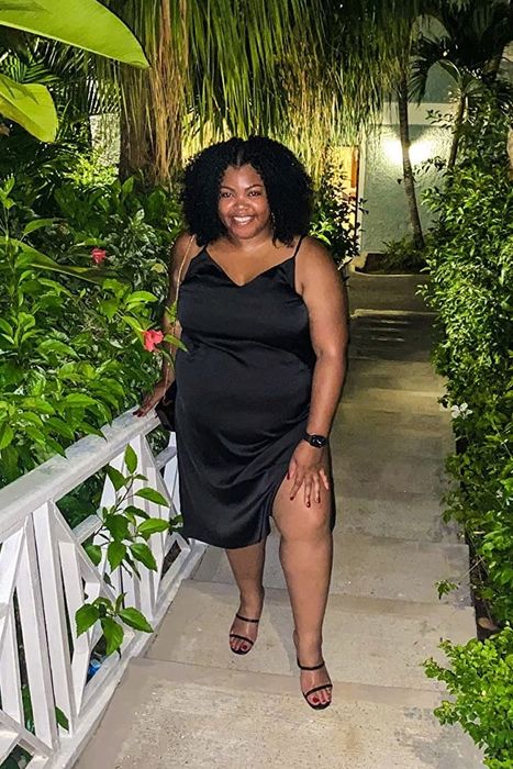 A reviewer poses in the black dress outside, showcasing the left-side slit that rises up to mid-thigh.