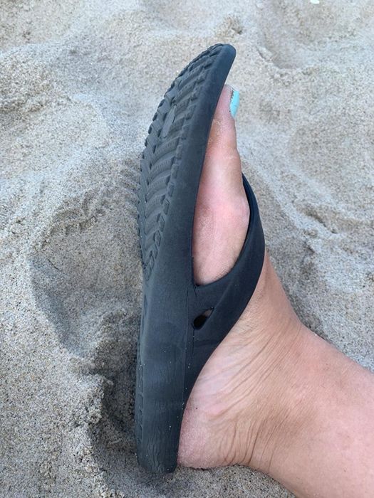 side view of the reviewer’s foot in black flip-flops on the sand, highlighting the flexible sole