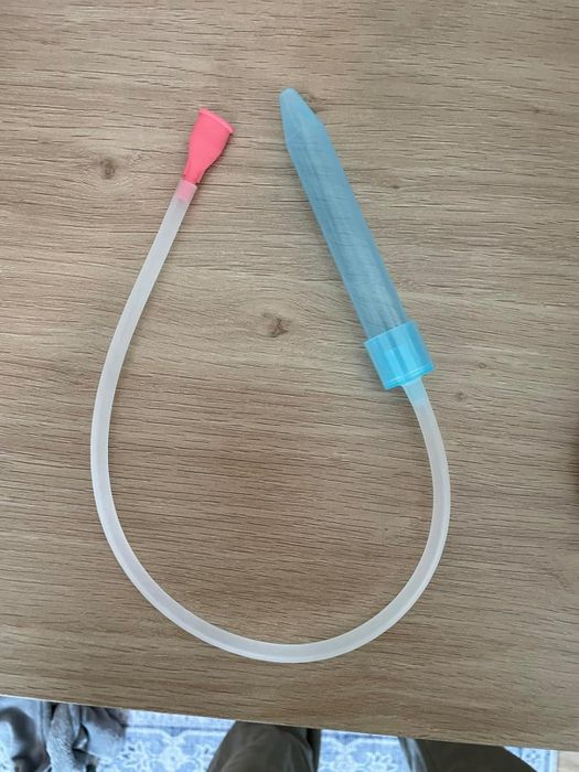 A flexible tube device featuring a bulb at one end and a pointed tip at the other, most likely a nasal aspirator, placed on a wooden surface.