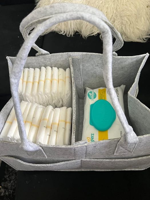 A felt organizer holding a pack of baby wipes and several stacks of diapers, placed on a sofa, perfect for nursery organization or travel convenience.