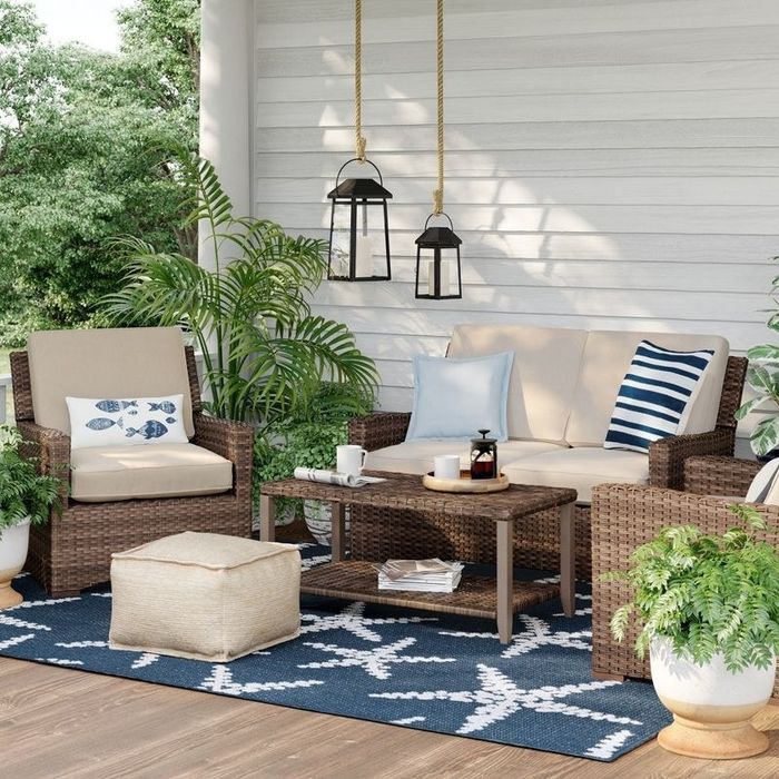 A tan loveseat on a deck accompanied by two matching armchairs and a coffee table.