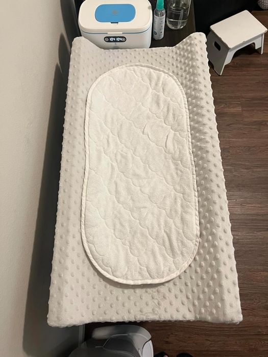 A changing table featuring a textured surface and a cushioned insert, positioned next to essential baby items.