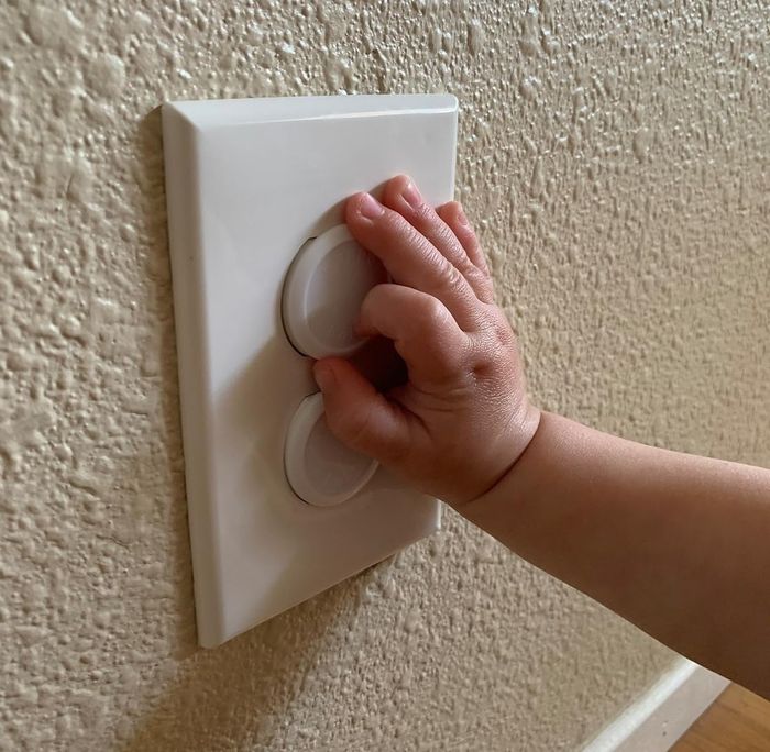 A child’s hand reaching for a light dimmer switch on a textured wall, illustrating home safety concerns.