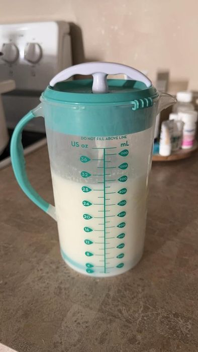 A container filled with liquid, marked with measurement lines in milliliters and ounces, resting on a kitchen counter.