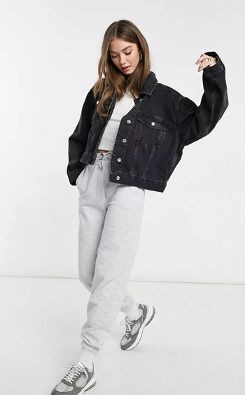 A model wearing a cropped oversized black denim jacket paired with gray sweatpants and a white crop top, set against a white background.