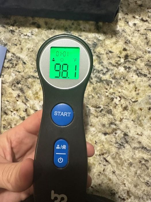 A digital thermometer displaying 98.1°F, held in hand, with buttons for start and settings visible.