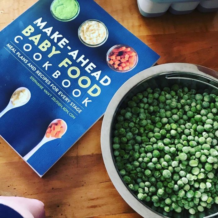 A cookbook titled 'Make-Ahead Baby Food,' placed next to a bowl of peas on a wooden table.