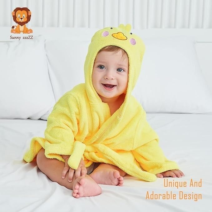 A baby wrapped in a duck-themed hooded bathrobe sits on a bed. Text: 