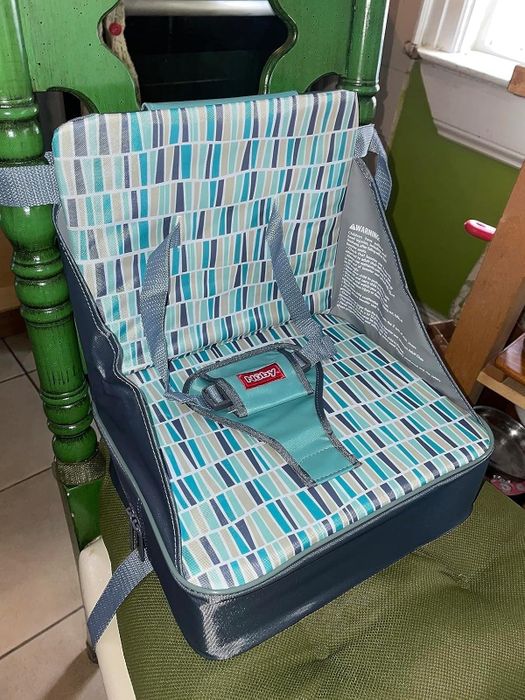 A portable booster seat featuring a geometric design on a kitchen chair, complete with safety straps and a buckle. Ideal for dining or travel purposes.