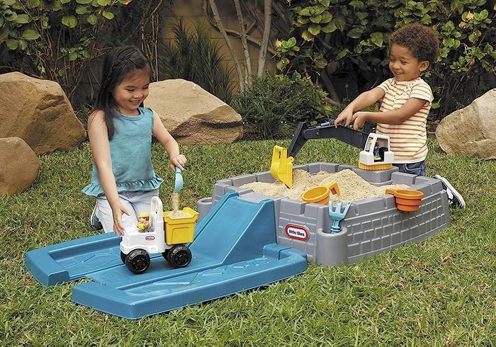 Two children playing with a blue and gray plastic sandbox, accompanied by yellow digging toys