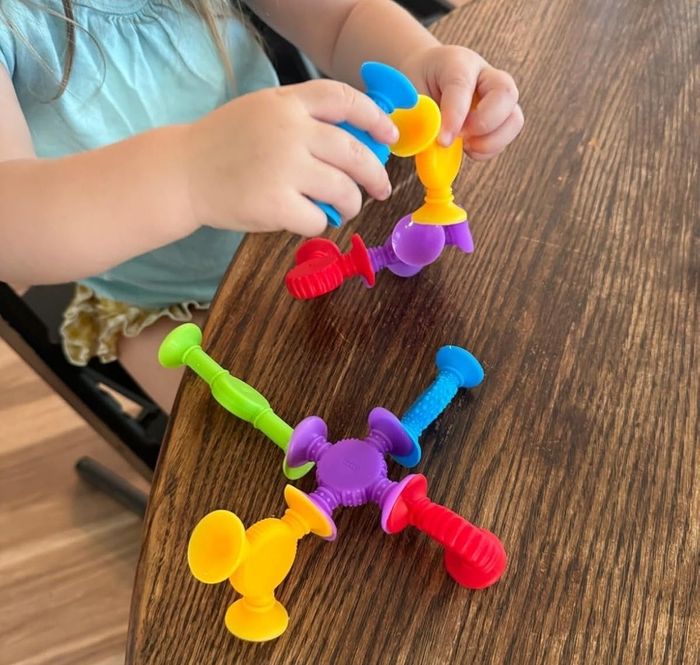 A child having fun with colorful suction toys on a wooden table.