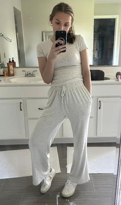 A woman takes a mirror selfie in a bathroom, wearing a casual matching loungewear set consisting of a short-sleeve top and drawstring pants.