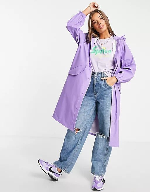 A model wears a long lavender raincoat, ideal for a stylish yet practical rainy day look.