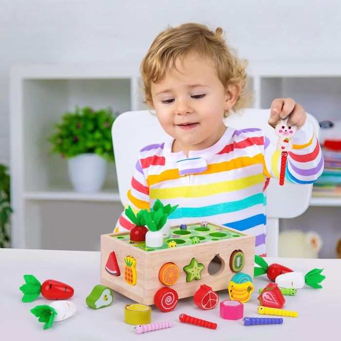A young child playing with a colorful wooden toy featuring fruits and vegetables, set on a table
