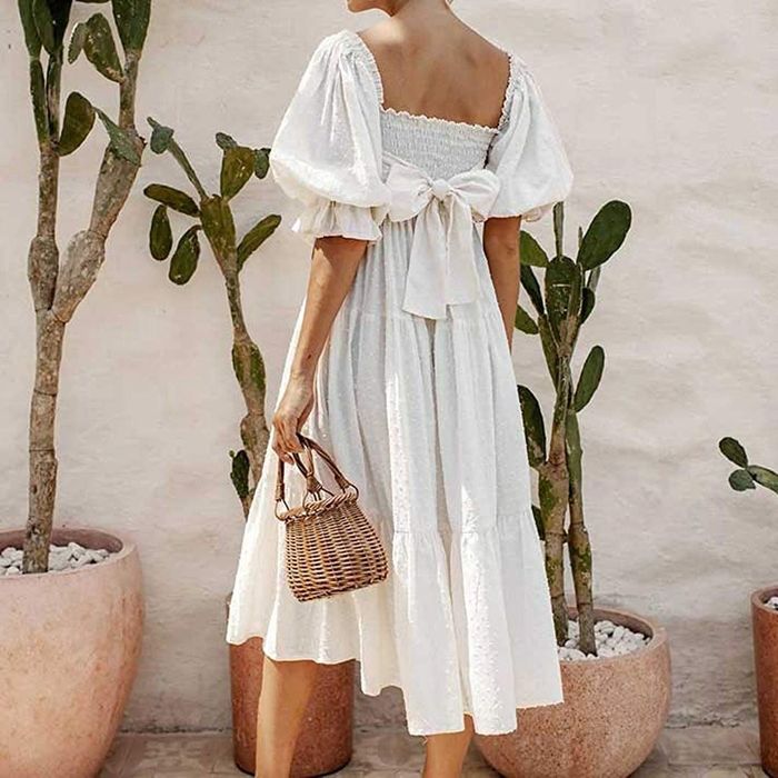 Another model presenting the back view of a white dress with a bow tied at the back