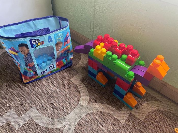 A big bag of Mega Bloks with 80 pieces, positioned next to a colorful dinosaur structure made from the blocks