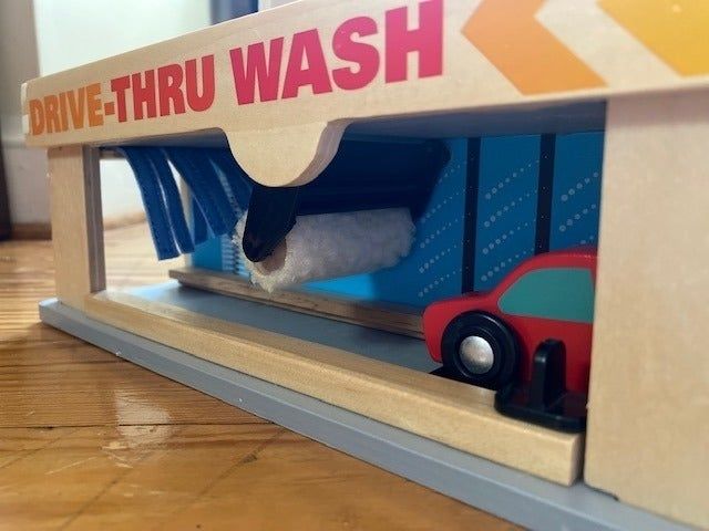 A toy car wash setup with a red toy car passing through, featuring foam brushes and a sign that reads 