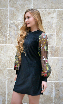 A reviewer dressed in a long-sleeve black dress featuring tulle embroidered sleeves