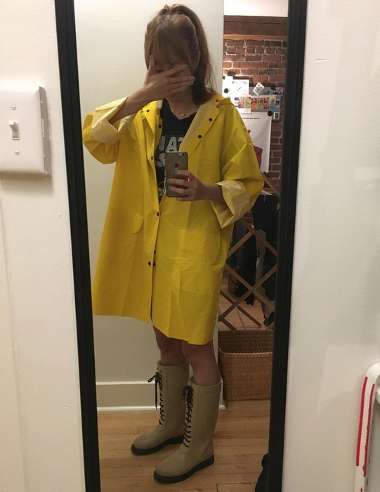 A reviewer takes a selfie while wearing an oversized yellow trench raincoat, capturing the bold look.