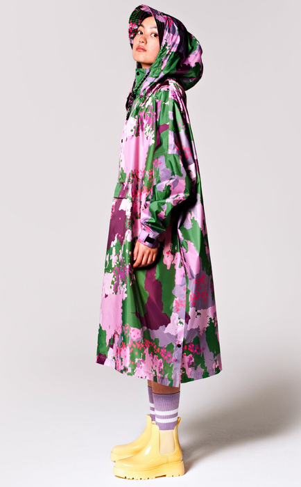 A model is sporting a long poncho in a spring camo pattern with shades of green and purple.