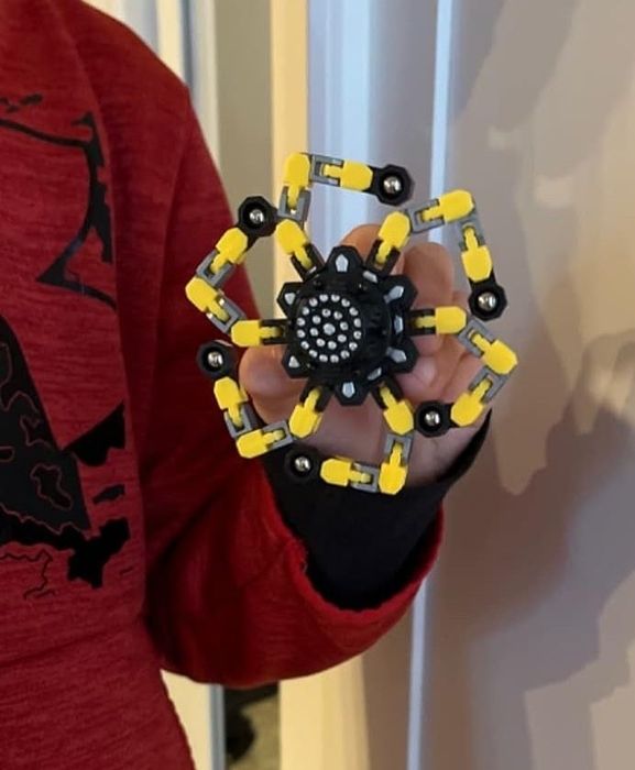A child holding a yellow and black toy spider model, wearing a red Under Armour hoodie