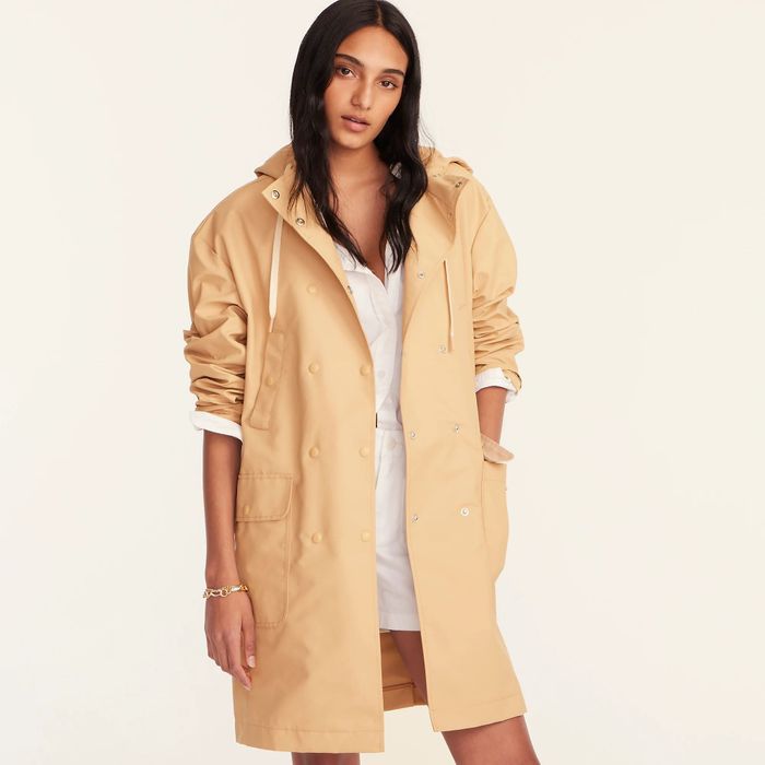 A model wears a sandy-colored double-breasted raincoat, showcasing its timeless appeal and sleek design.