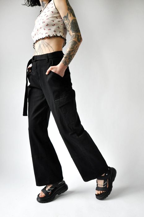A model demonstrates black cargo pants with a coordinating belt, captured from the side.