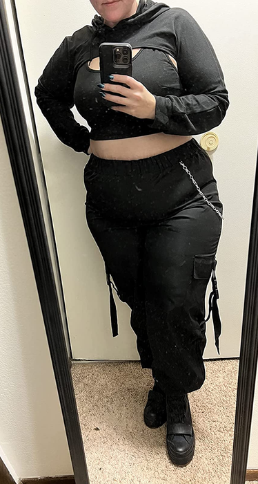 A reviewer takes a mirror selfie wearing black cargo pants adorned with a chain.