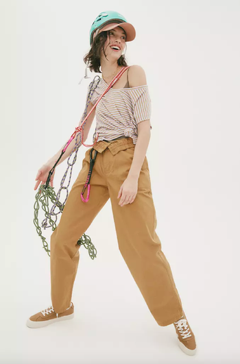 Model wearing the pants, folded at the waistband, in a gold color