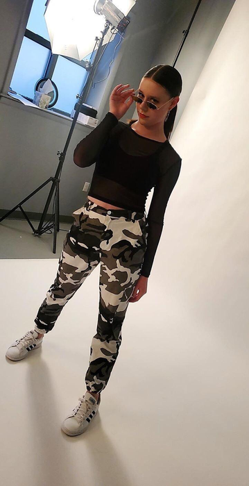 A reviewer modeling the pants in a professional photography studio, styled in camouflage.