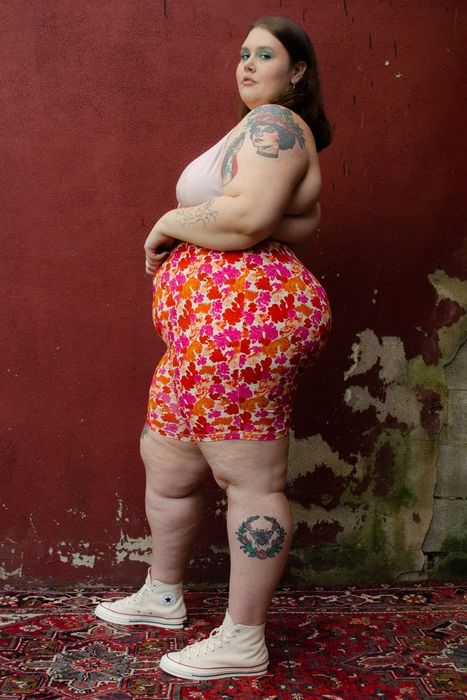 A side view of a plus-size model wearing pink and orange floral bike shorts.