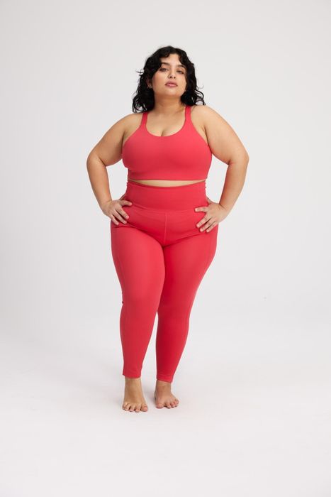 A model donning bright pink-red leggings, matched with a coordinating sports bra for a vibrant workout look.