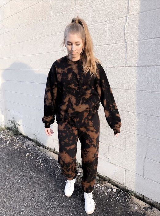 A model sports a matching black and brown bleached sweatshirt and sweatpants set, paired with white sneakers.