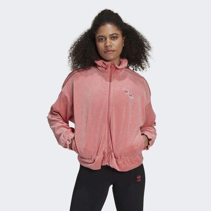 A model sports a dusty pink velour Adidas zip-up jacket, complemented with matching track pants for a relaxed yet stylish look.