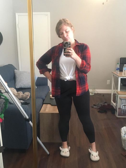 A reviewer dressed in black opaque leggings, paired with a flannel shirt, white T-shirt, and bunny slippers.