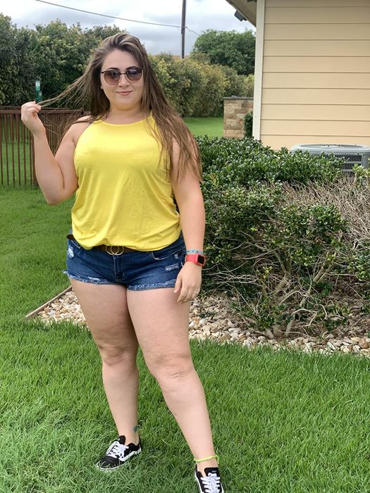 A reviewer showcasing a yellow tank top paired with denim shorts and Vans sneakers.
