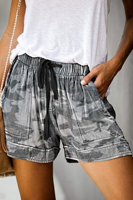 The model is seen in olive green camouflage linen shorts, offering a laid-back yet fashionable look.