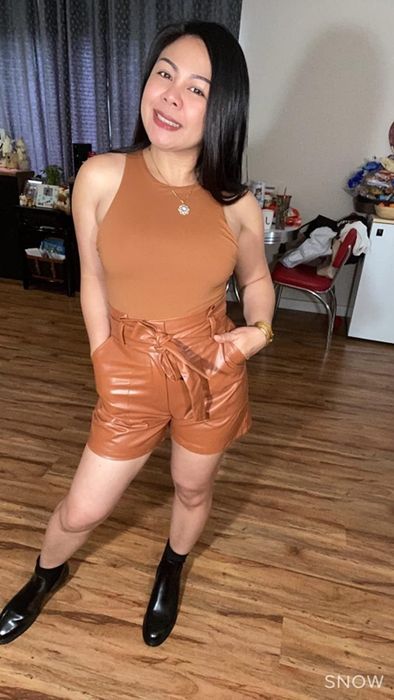 A reviewer rocks a tan bodysuit with faux leather tan shorts and black boots for a bold, stylish look.