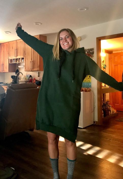 Another reviewer wears the same hoodie dress, but in a dark green color, while lounging at home.