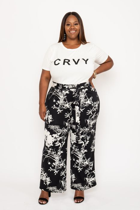 A plus-size model rocks black printed wide-leg pants paired with a white tee that features the word