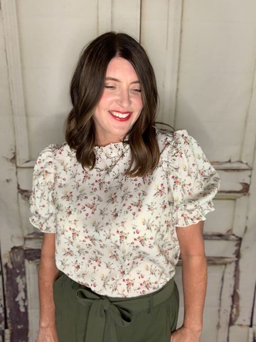 A reviewer rocking a white puff-sleeve blouse adorned with tiny pink flowers