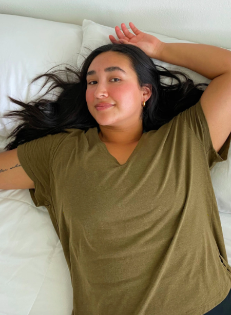 The model is lounging on a white bed wearing a green V-neck tee.