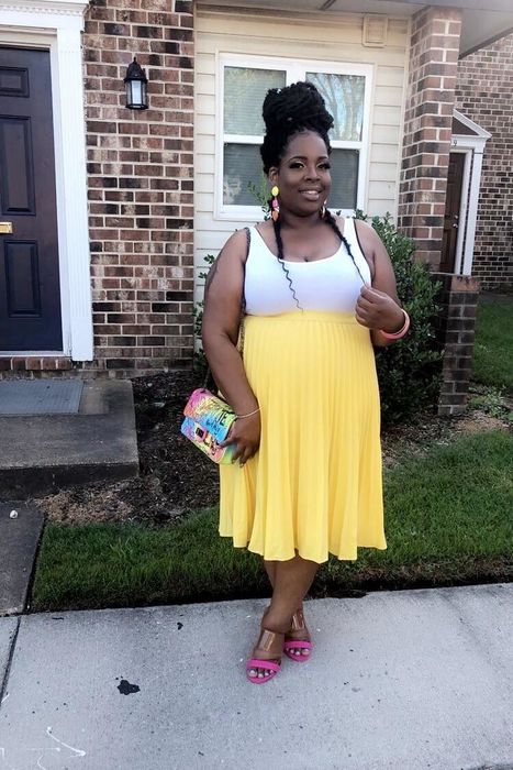 The reviewer is sporting a yellow skirt, white tank top, and heels.