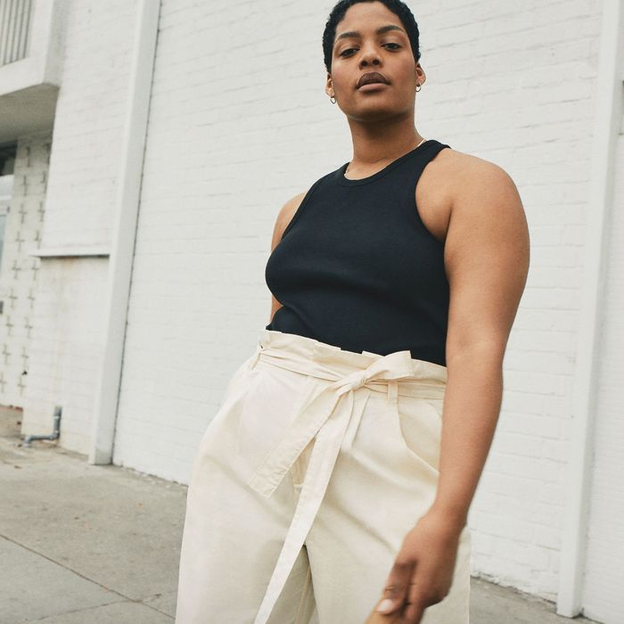 A model sporting a black tank top and cream-colored tie-waist pants