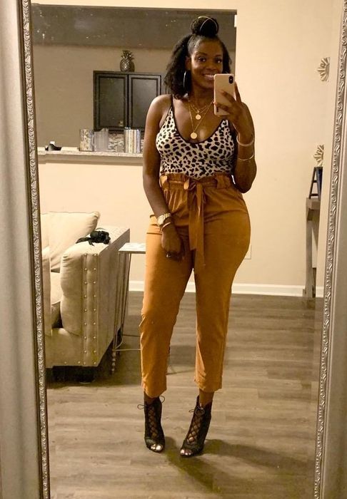 A reviewer shows off mustard-colored pants paired with a stylish tank top and black strappy heels.
